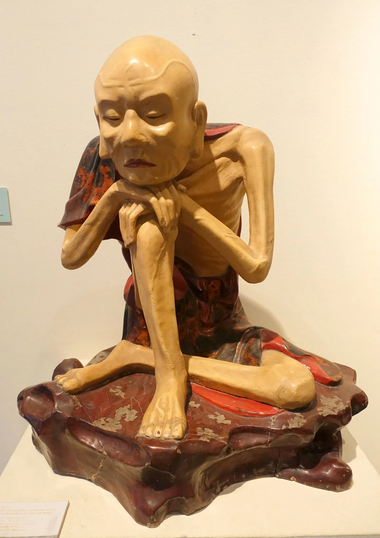 Ảnh chụp pho tượng gỗ sơn tạc một vị tu hành gầy guộc ngồi thiền trên bệ sơn đỏ